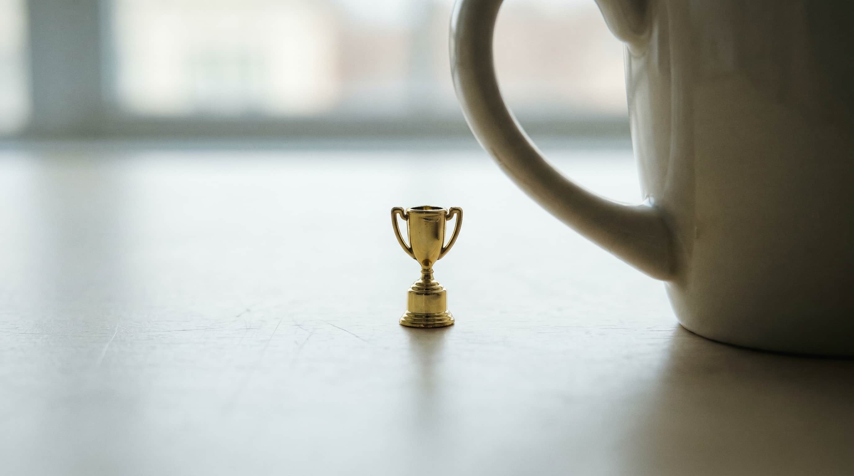 A gold trophy shrunk to the size of a thumbnail, alone on a desk, dwarfed by an ordinary coffee mug. The award for the work nobody sees.